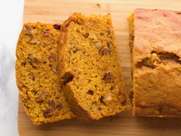 Overhead Shot - sliced pumpkin spice cake loaf on a wooden cutting board on marble countertop.