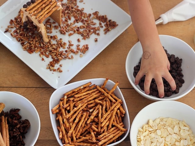 Young hand reaching into bowl of food items to decorate mini sukkah.