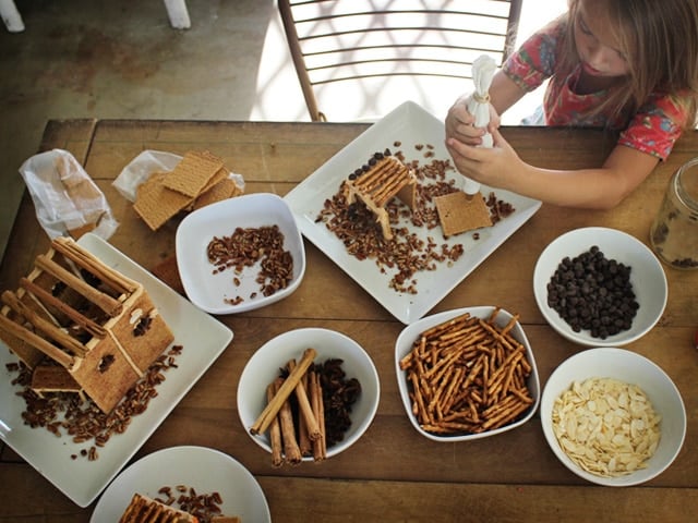 Table full of food items to decorate mini sukkah - pretzels, chocolate chips, and whole spices.