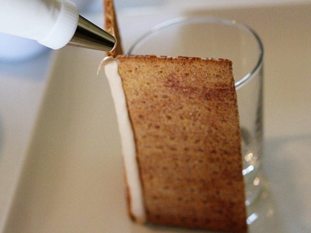 Royal icing being applied with a decorating tip to graham cracker walls of mini sukkah.