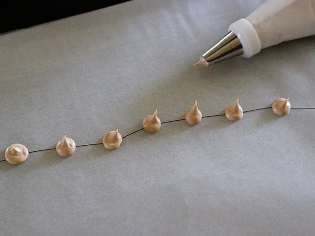 Royal icing in drops on a string on wax paper to make small decoration. 