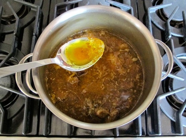 Skimming fat from the surface of the lamb stew.