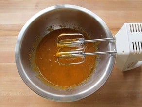 Beating sugar, eggs, and oil with a hand mixer.
