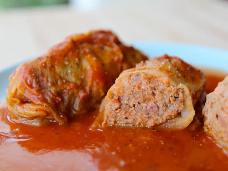 Two stuffed cabbage leaves, one cut in half, on a blue plate with sauce.