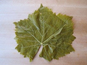 Grape leaf on a cutting board with vein side up.