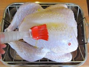 Brushing raw turkey with olive oil.