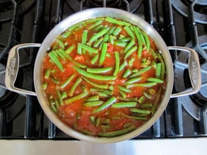 Simmering green beans in tomato sauce in a skillet.