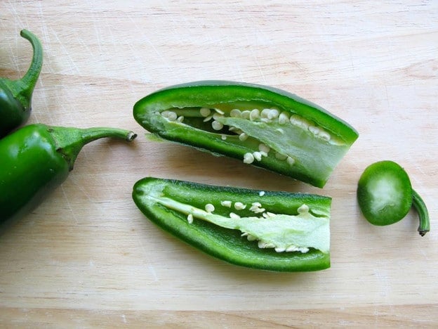 Jalapeno halved with seeds on cutting board.