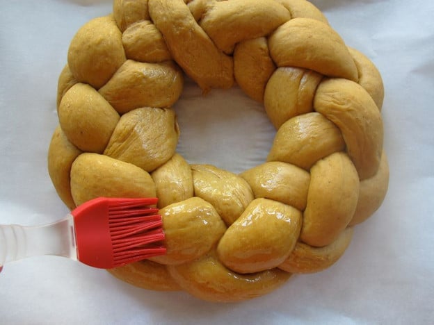 Brushing eggwash over braided challah circle.