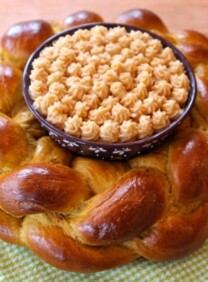 Horizontal close-up of a pumpkin challah centerpiece with honey butter, resting on a green checkered table napkin.