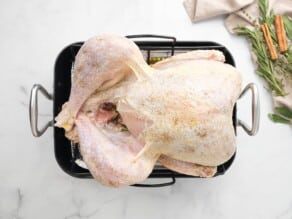 Overhead shot of a seasoned raw turkey sitting on top of a roasting pan rack.