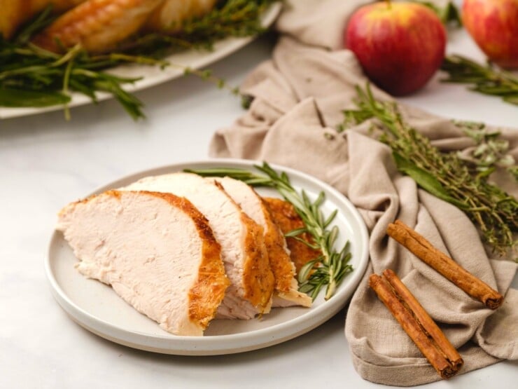 Horizontal shot of a decorative table containing a plate of sliced turkey, a cloth napkin, and various dried herbs and spices.