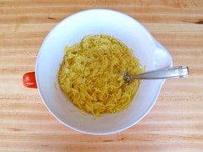 Egg stirred into shredded potatoes in a bowl.