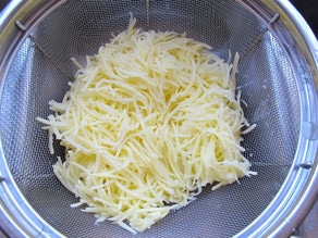 Shredded potatoes draining in a colander.