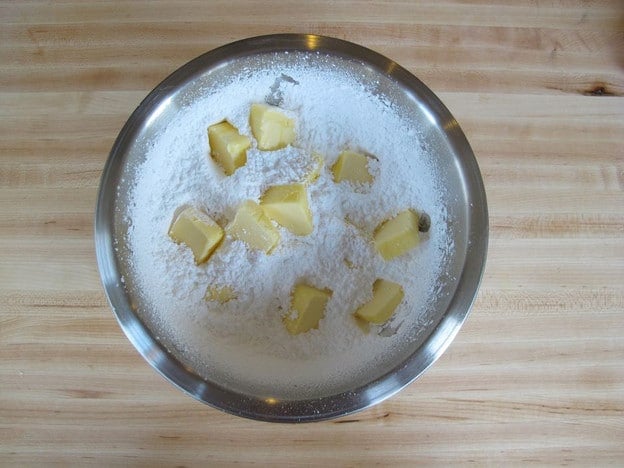 Cubed butter in bowl of powdered sugar.