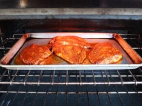 4 flat pounded chicken breasts on a baking sheet coated in marinade, bubbling beneath a hot broiler in the oven.