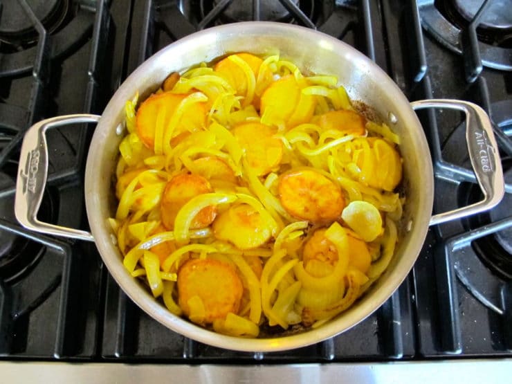 Sliced potatoes and onions in a large saute pan.