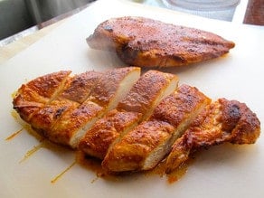 Paprika chicken breasts sliced on a cutting board.