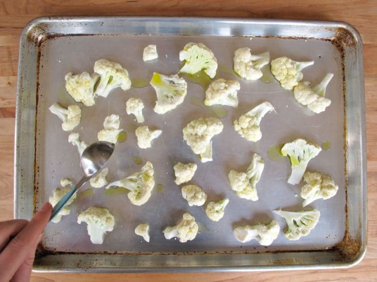 Drizzling olive oil over cauliflower florets on a baking sheet.