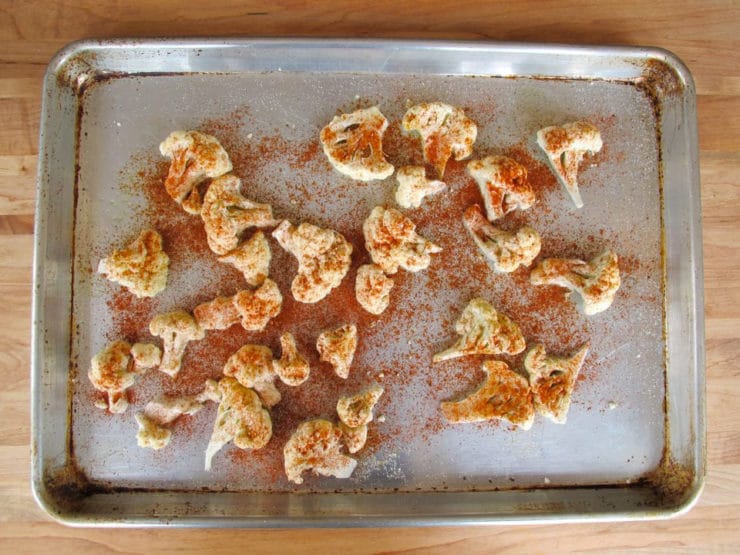 Cauliflower florets on a baking sheet, coated with paprika and salt.