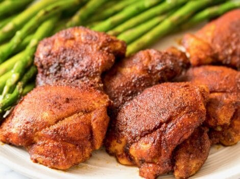 Square Crop - Smoked Paprika Chicken Thighs with boneless skinless thighs, roasted asparagus in background, on a white plate on a white marble countertop.