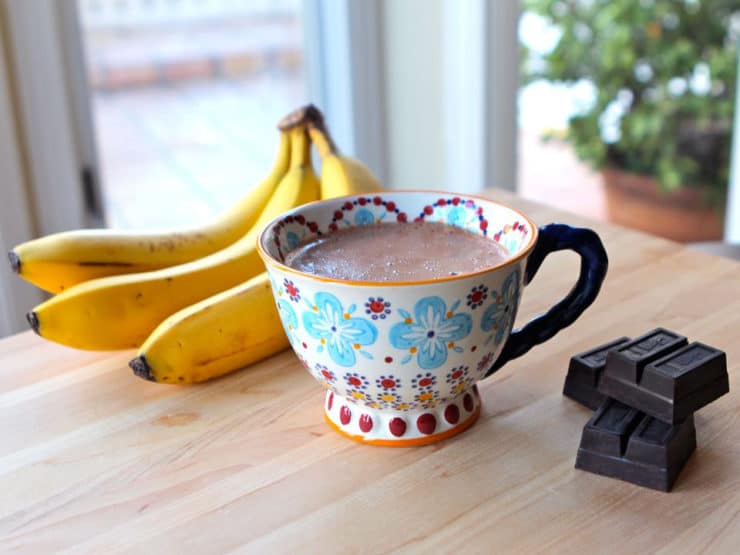 Banana Hot Chocolate served in a fancy colorful cup with block of chocolate and three bananas in each side