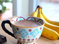 A cup of banana hot chocolate with bananas on the background
