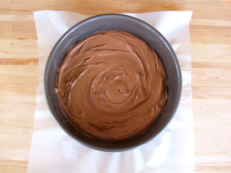 Cheesecake batter spread into parchment lined springform pan.