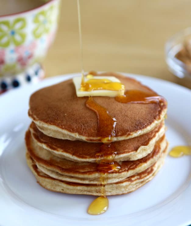 Close up of pancakes with butter and maple syrup on white plate.