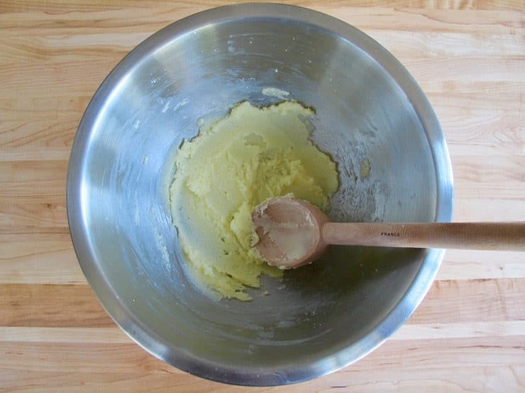 Butter and sugar creamed in stainless steel mixing bowl on wooden background.
