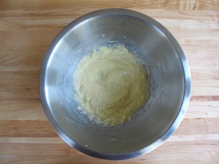 Butter and sugar creamed with egg in stainless steel mixing bowl on wooden background.