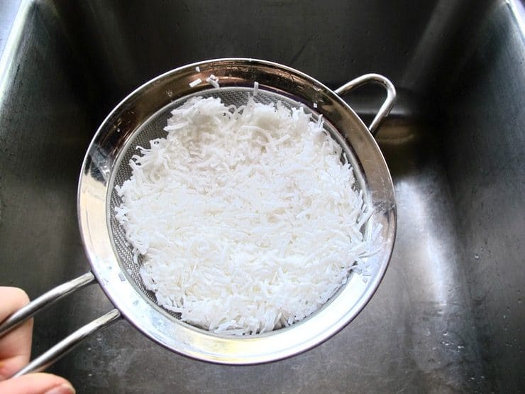 Coconut shreds draining in wire mesh strainer.
