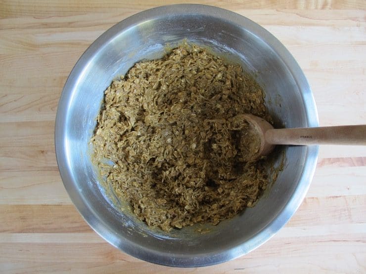 Molasses cookie dough in stainless steel mixing bowl mixed with wooden spoon.