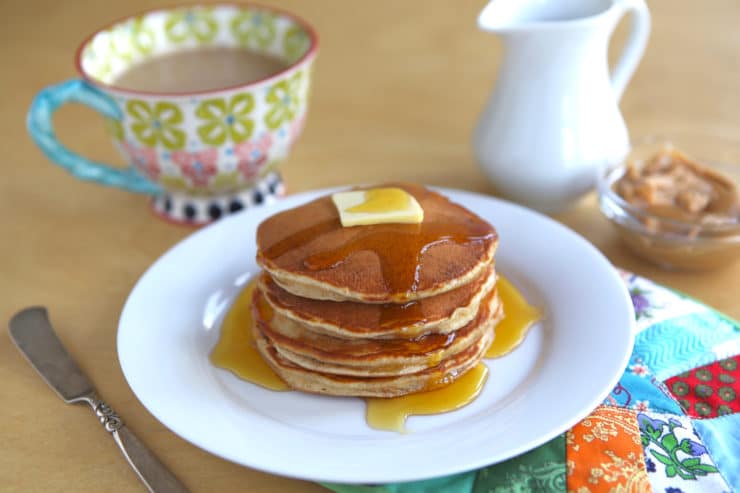 Peanut butter pancakes on white plate with butter and maple syrup, served with coffee.