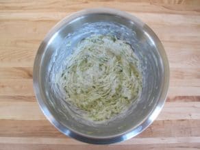 Cream cheese and cucumber shred mixture in stainless steel bowl on wooden background.