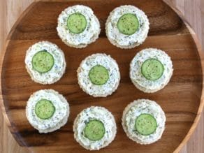 Overhead view - platter of cucumber rye open faced finger sandwiches, crustless, with pepper on a wooden background.