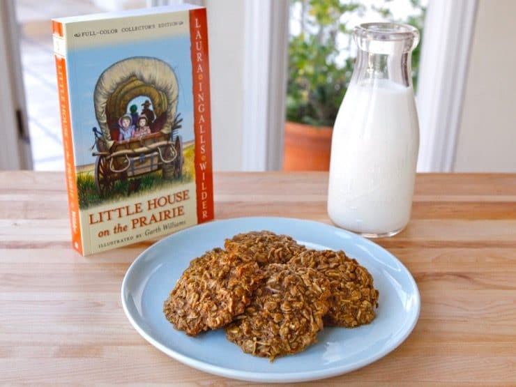 Wide shot - plate of 4 molasses cookies with Little House on the Prairie book and bottle of milk in background. 