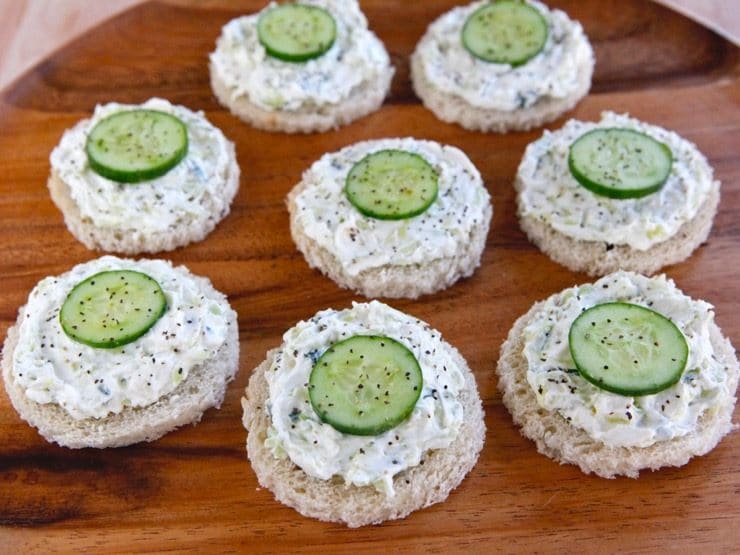 Platter of cucumber rye open faced finger sandwiches, crustless, with pepper on a wooden background.