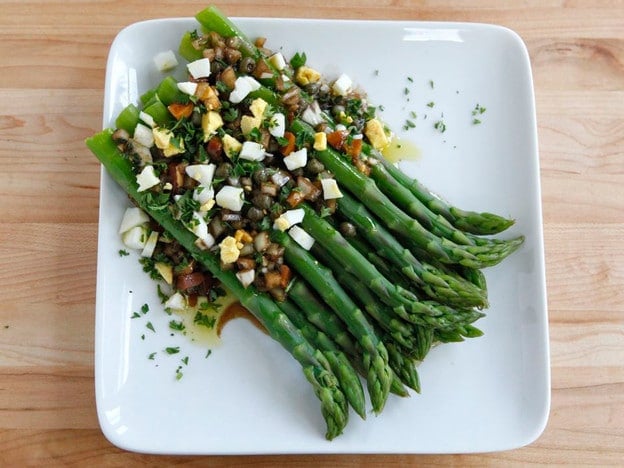 Overhead shot of Marinated Asparagus with hard cooked egg, capers, and herbs served on a white square plate.