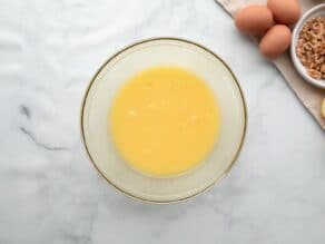 Horizontal overhead shot of a glass mixing bowl containing a beaten egg yolk mixture.