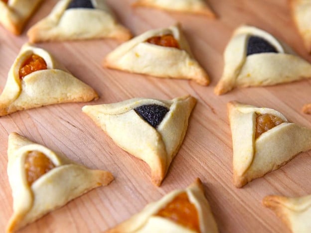Image of triangular buttery hamantaschen dough with yellow and dark purple filling.