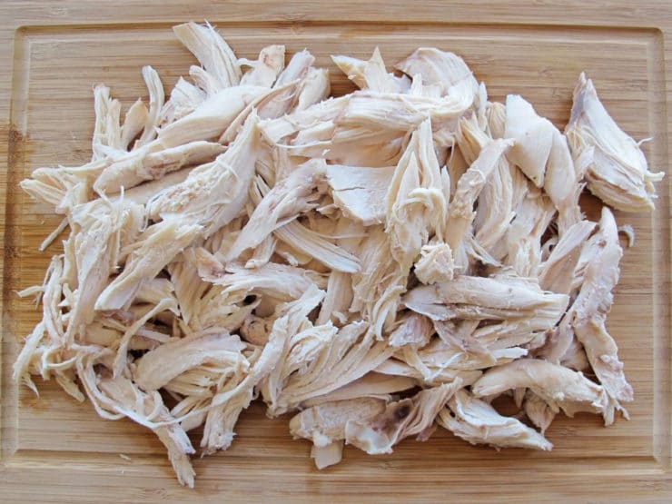 Pulling apart cooked chicken into bite-size pieces.