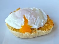 Poached egg on toasted English muffin broken with yolk dripping out.
