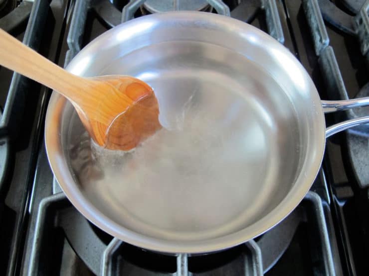 Wooden spoon stirring to create whirlpool in saucepan with lightly simmering water on stovetop.