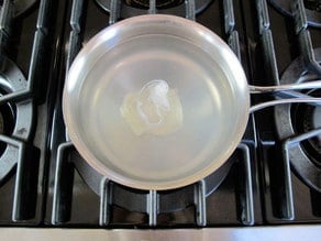 Single poached egg in center of saucepan with lightly simmering water on stovetop.