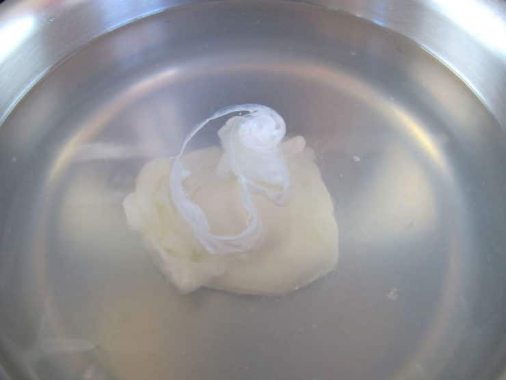 Close up of single poached egg in saucepan with lightly simmering water on stovetop.