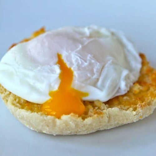 Poached egg on toasted English muffin broken with yolk dripping out.