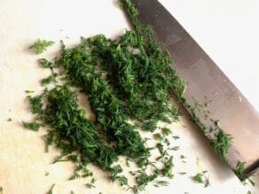 Fresh dill chopped with chef's knife on white cutting board.