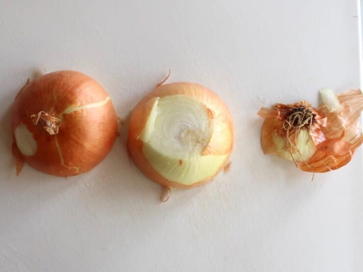 Yellow onion sliced in half on white cutting board, root end removed.
