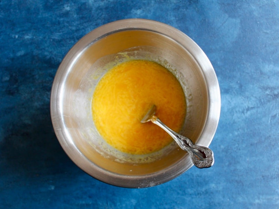 Egg yolks and schmaltz stirred together with a fork in a stainless bowl on a blue counter.